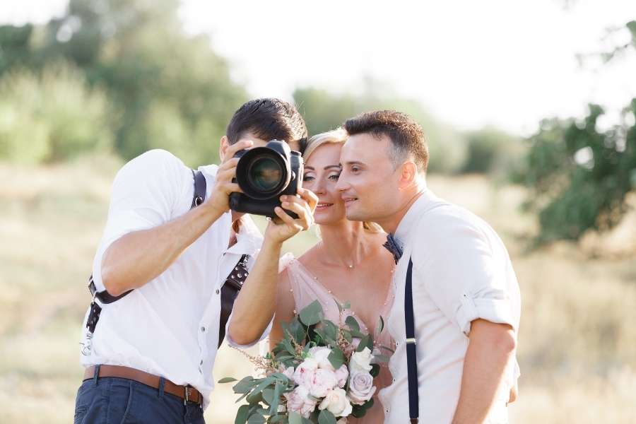 Un photographe de mariage professionnel prend une photo en gros plan d'un couple souriant en extérieur lors d'une séance photo.